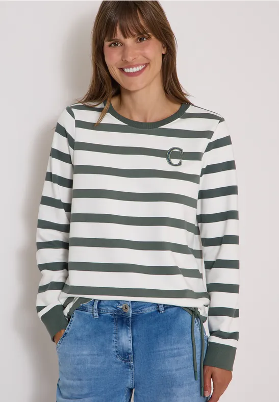 Femme souriante en chemise à rayures blanc-vert et jean.