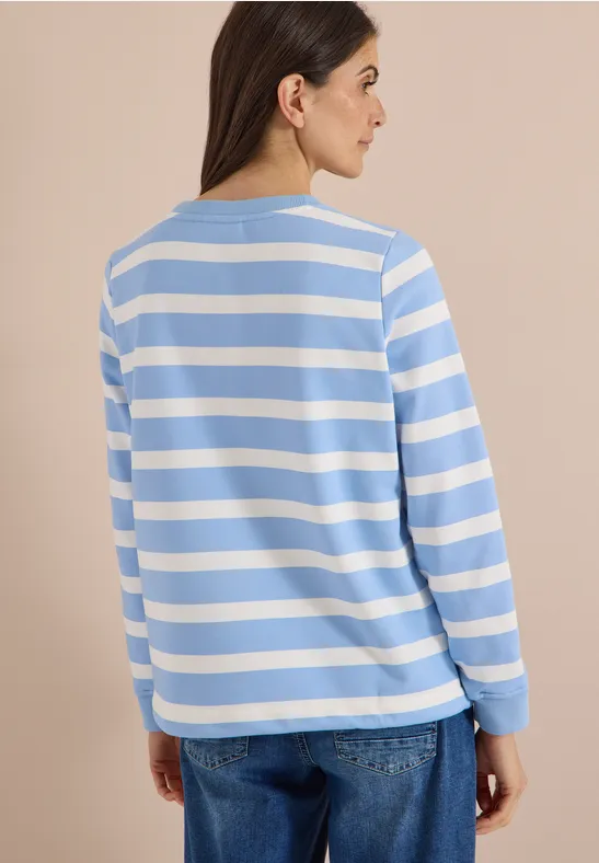 Frau von hinten in blau-weiß gestreiftem Langarmshirt und Jeans vor beigem Hintergrund.