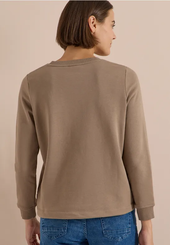 Frau von hinten trägt taupefarbenen Pullover und blaue Jeans