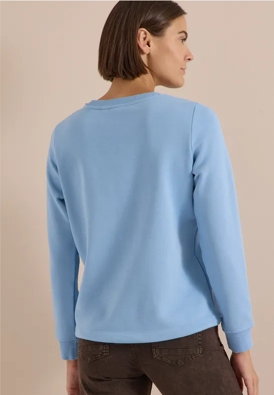 Frau von hinten in hellblauem Pullover, schlichtes Design und neutraler Hintergrund.