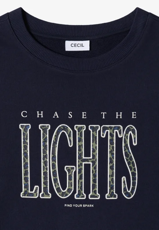 Czarny T-shirt z napisem „CHASE THE LIGHTS FIND YOUR SPARK” białymi, dekoracyjnymi literami.