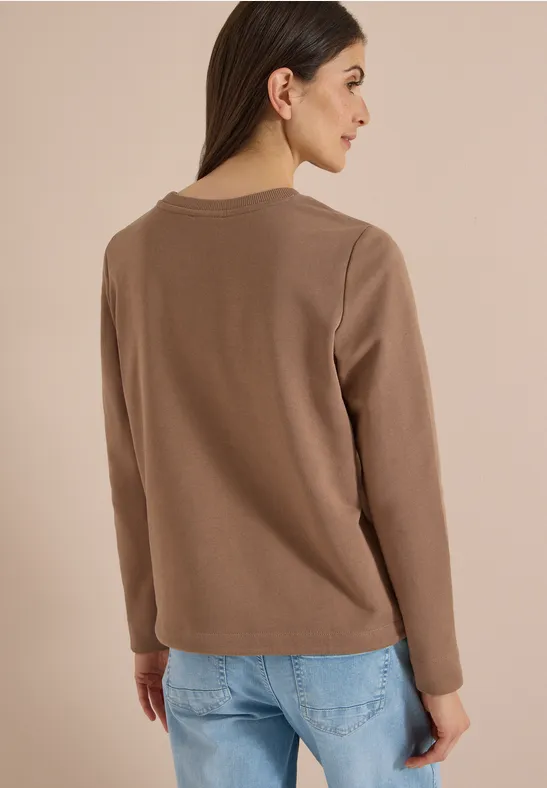 Rückansicht einer Frau, die ein langärmeliges, braunes Oberteil und blaue Jeans trägt.