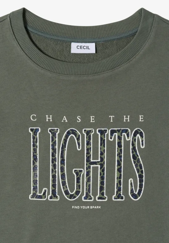 Olivegrünes T-Shirt mit Markenlabel und großer Aufschrift 'CHASE THE LIGHTS' in gemusterten Buchstaben.