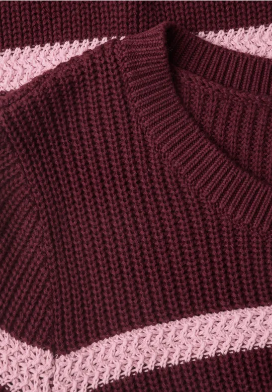 Close-up van een gebreide trui in bordeauxrood met roze horizontale strepen.