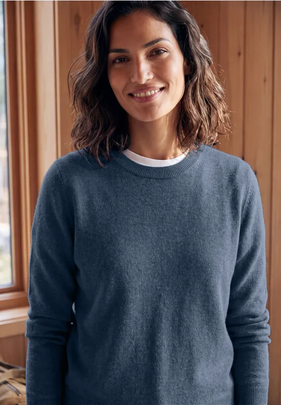 Femme souriante en pull bleu devant un mur en bois