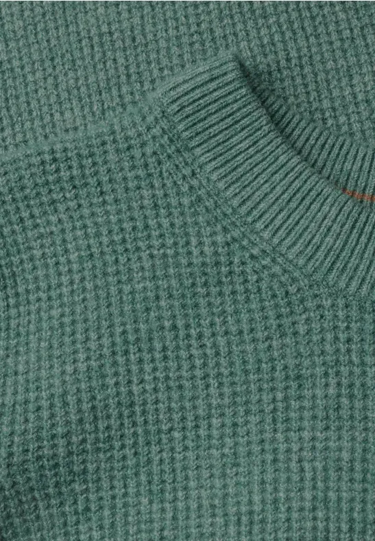 Nahaufnahme eines grünen Pullovers aus grobem Rippstrick mit Rundhalsausschnitt.
