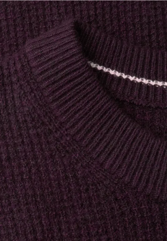Nahaufnahme eines dunkelvioletten Rippstrick-Pullovers mit feinem weißen Nahtdetail im Kragen.