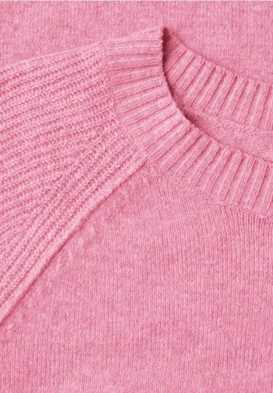 Close-up van een roze gebreide trui met ronde hals en fijne textuur.
