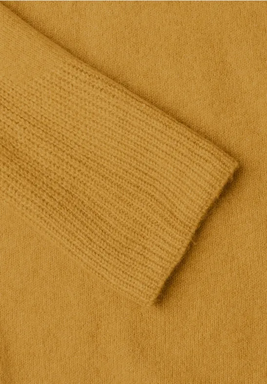 Nahaufnahme eines senfgelben Strickpullovers mit Ärmel und Körper in sanfter Textur.