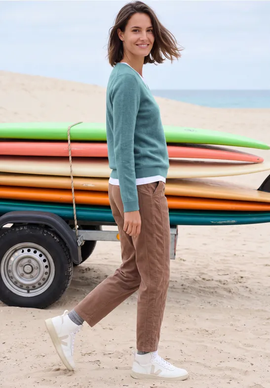Een lachende vrouw op het strand naast kleurrijke surfplanken, casual gekleed.