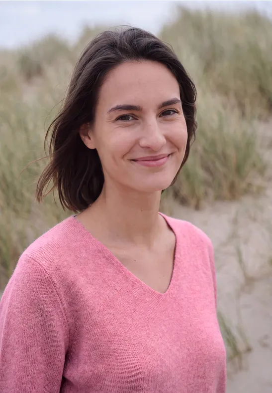 Een glimlachende vrouw in een roze trui voor de duinen op het strand