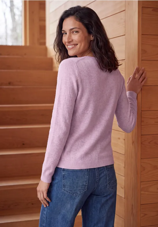 Eine lächelnde Frau mit rosa Pullover und Jeans steht auf einer Holzwendeltreppe und schaut zurück.