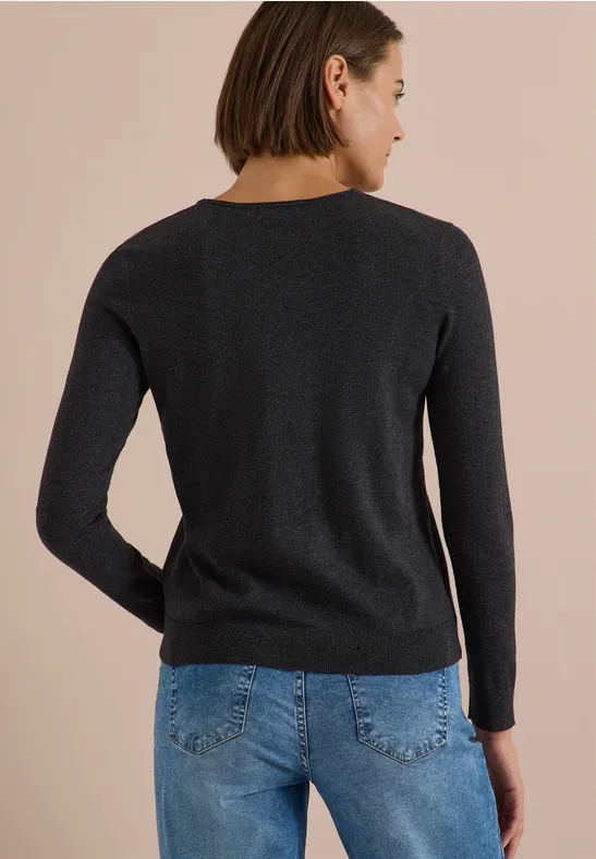 Rückansicht einer Frau in schwarzem Pullover und blauen Jeans vor hellem Hintergrund.
