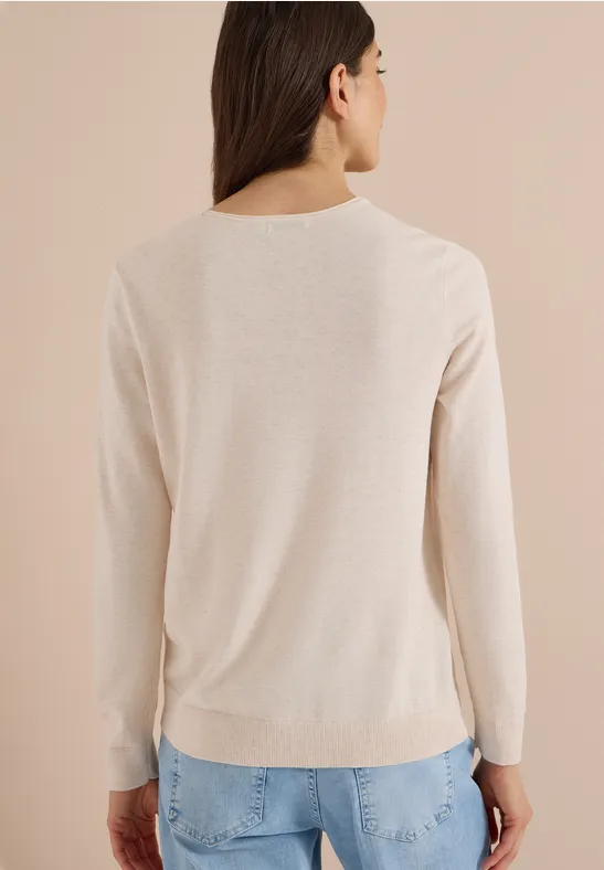 Frau von hinten in beigem Pullover und blauer Jeans vor hellem Hintergrund.