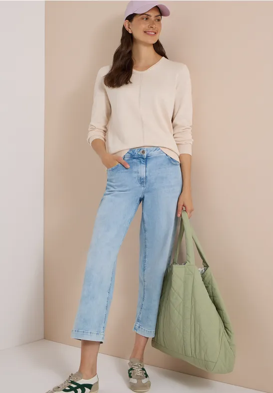 Frau in beigem Pullover, weitem Jeans, Basecap und grünem Stepp-Shopper