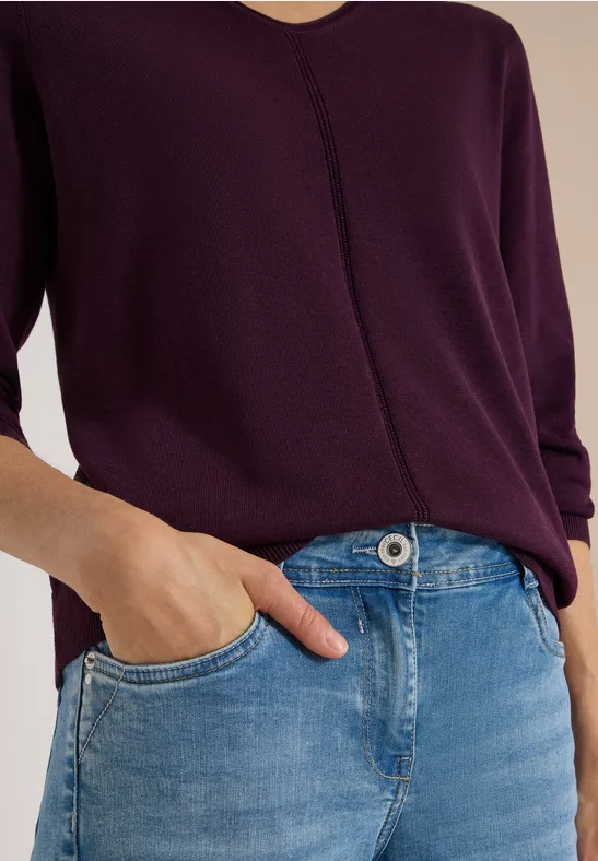 Violettes Langarmshirt und blaue Jeans, Hand lässig in der Tasche.