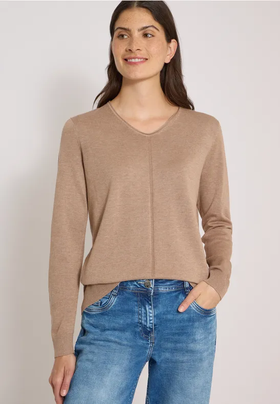 Eine lächelnde Frau in braunem Pullover und blauen Jeans.