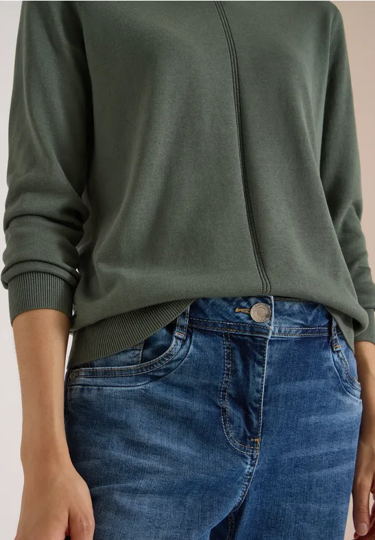 Oberkörper einer Person in grünem Pullover und blauen Jeans.