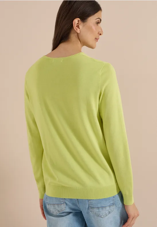 Eine Frau trägt von hinten gesehen einen hellgrünen Pullover vor neutralem Hintergrund.