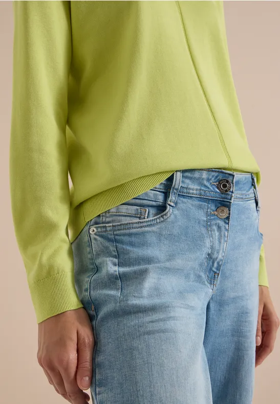 Person trägt hellgrünen Pullover und hellblaue Jeans, Bildausschnitt auf Torso und Arme.