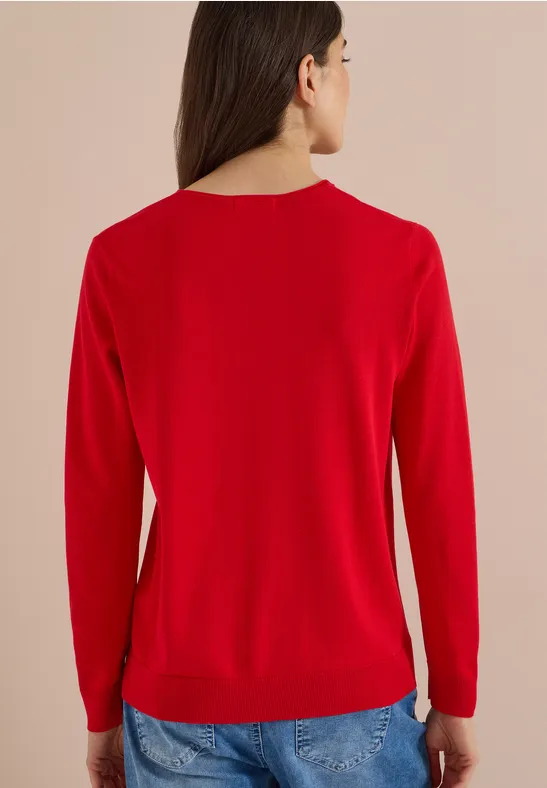 Frau in rotem Pullover und Jeans, gesehen von hinten.