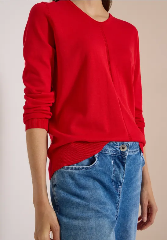 Eine Person in rotem Pullover und blauen Jeans, nur Oberkörper und Arme sichtbar.