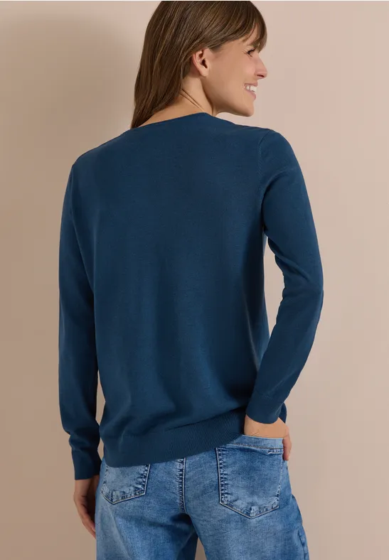Frau von hinten in dunkelblauem Pullover und Jeans, Hände in den Taschen.