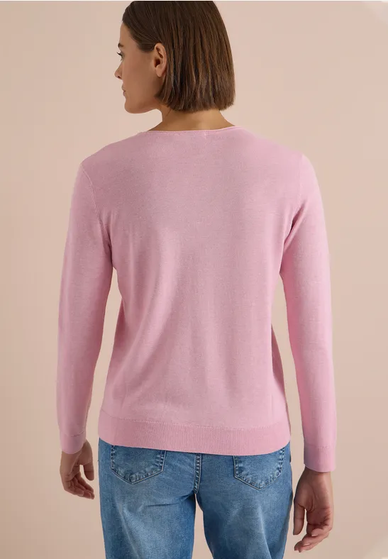 Frau mit kurzem Bob trägt rosa Pullover und blaue Jeans, Rückansicht.