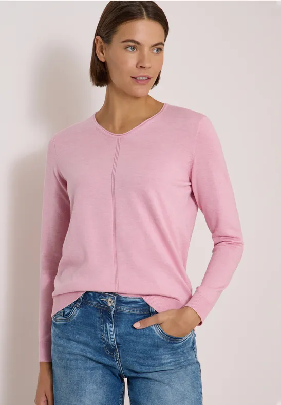 Frau in rosa Pullover und Jeans, entspannte Pose mit Hand in Hosentasche