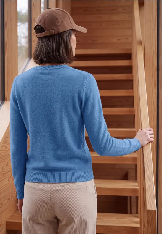 Achteraanzicht van iemand met blauwe trui en pet die een houten trap opgaat.