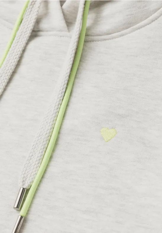 Nahaufnahme eines hellgrauen Hoodies mit hellgrünen Kordeln und kleinem hellgrünem Herzlogo.