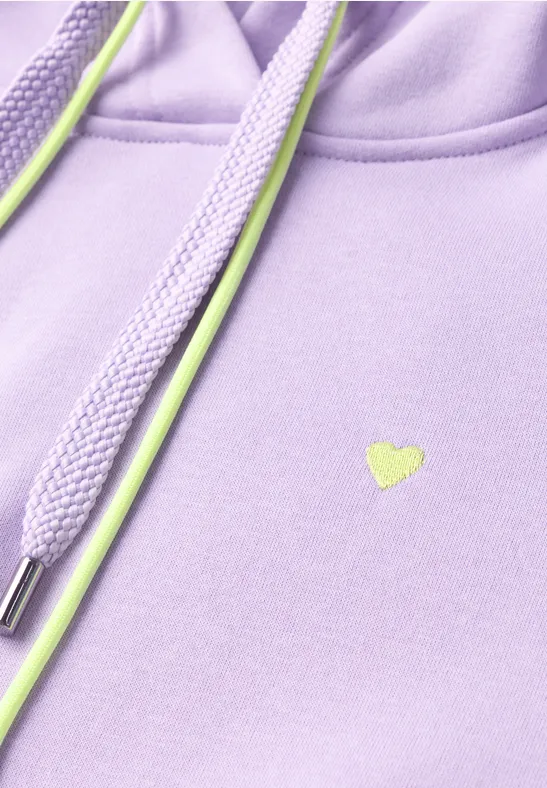 Fliederfarbene Kapuzenjacke mit neongrünen Kordeln und kleinem Herzlogo in Nahaufnahme.