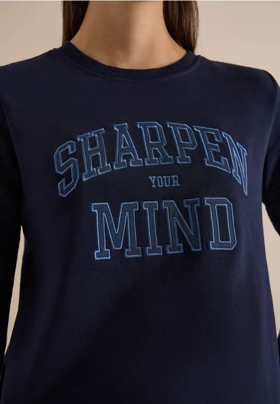 Person trägt dunkelblaues T-Shirt mit der Aufschrift 'SHARPEN YOUR MIND'