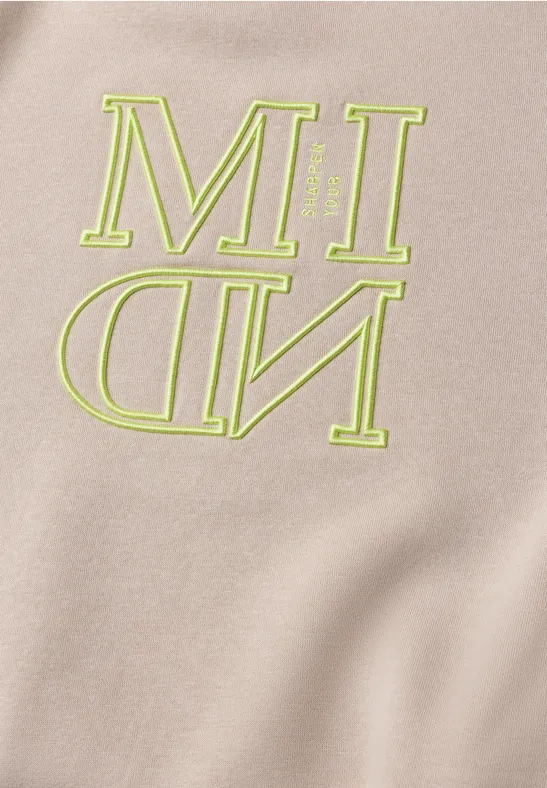 Beige Stoff mit neongrüner Aufschrift 'MIND', wobei 'ND' spiegelverkehrt dargestellt ist.