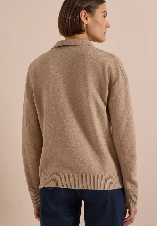Femme de dos portant un pull beige et un pantalon foncé, regard tourné sur le côté.