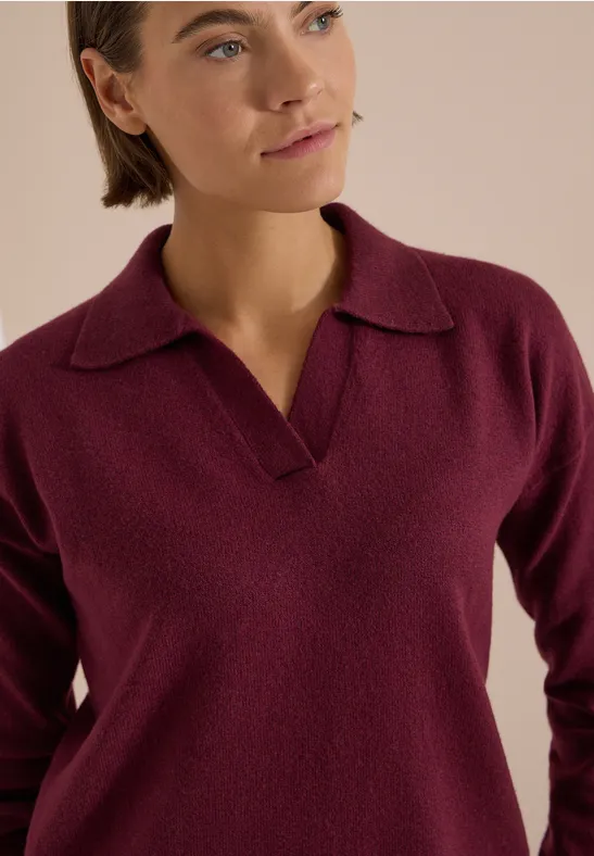 Une femme porte un pull bordeaux à col polo.