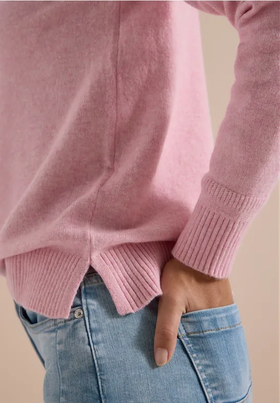 Person im rosa Pullover und blauen Jeans, Hand steckt seitlich in der Gesäßtasche.