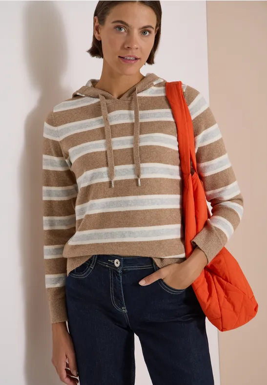 Jeune femme en sweat à capuche rayé, jean et sac orange devant un fond clair.