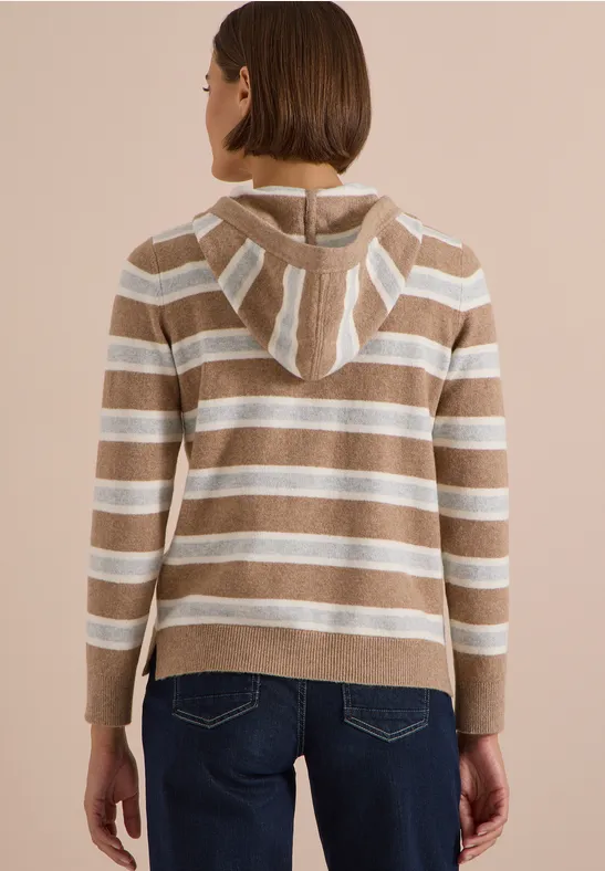 Femme de dos portant un sweat à capuche beige et blanc à rayures, associé à un jean bleu.