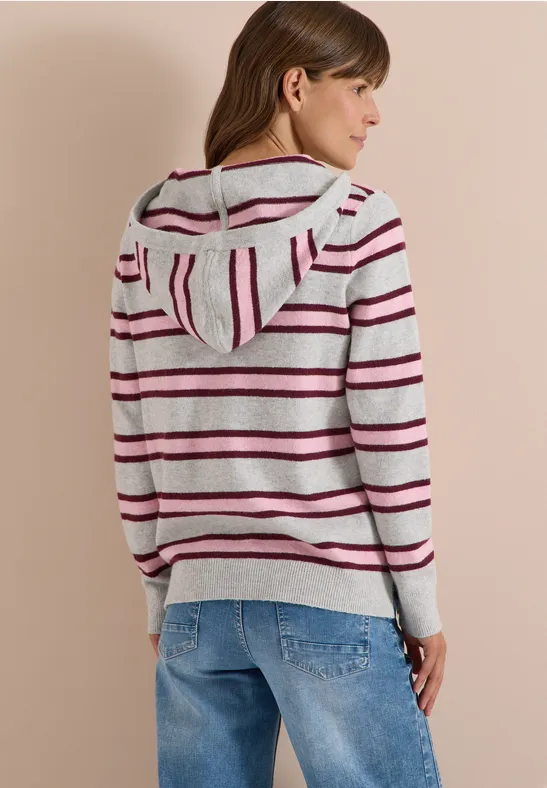 Frau in grauem Kapuzenpullover mit bunten Streifen und Jeans, Rückansicht im Halbprofil.