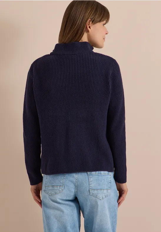 Femme vue de dos en pull en maille bleu marine à col montant et jean clair.