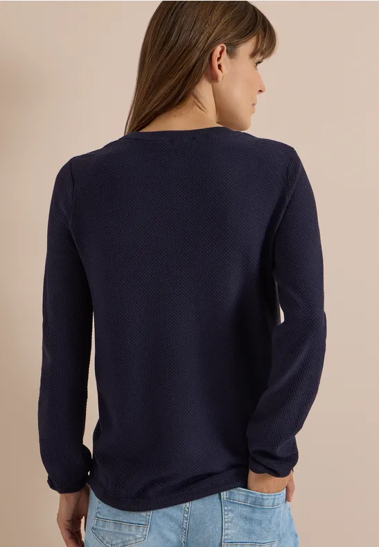 Femme de dos en t-shirt bleu marine à manches longues sur fond clair.