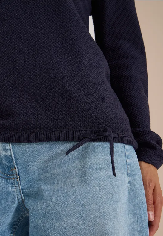 Pull texturé bleu foncé à cordon latéral, associé à un jean bleu clair.