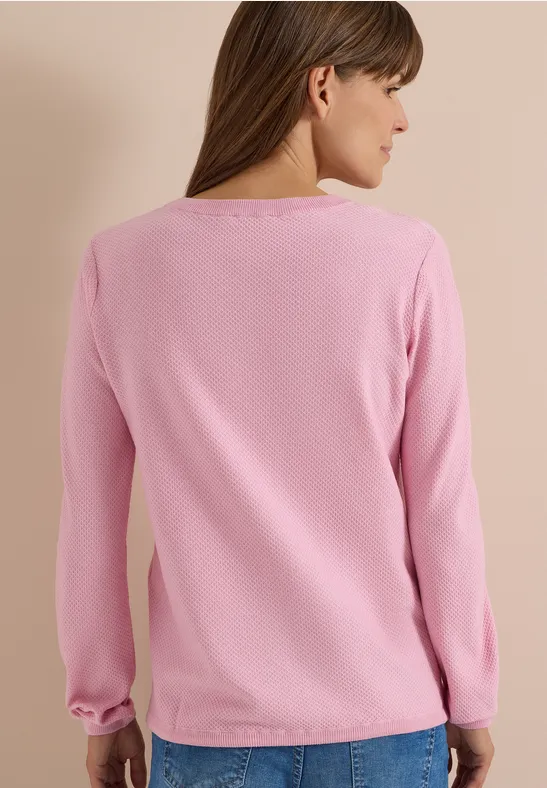 Vue de dos d'une femme portant un pull rose à manches longues et un jean bleu sur fond neutre.