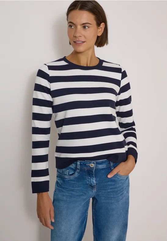 Frau mit dunkelblau-weiß gestreiftem Pullover, blauer Jeans und kurzen braunen Haaren.