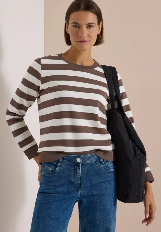 Brünette Frau trägt braun-weiß gestreiftes Shirt und blaue Jeans mit schwarzer Tasche.