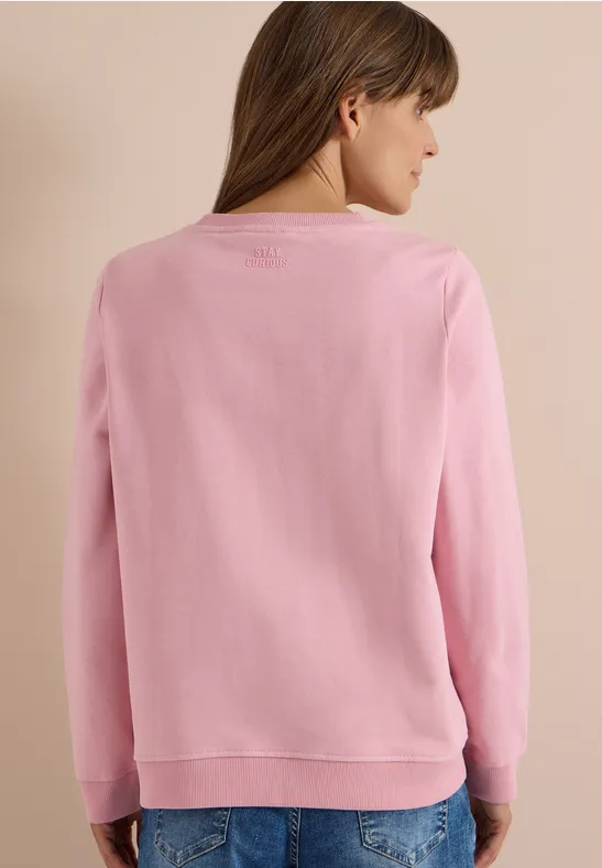 Vue de dos d'une femme portant un pull rose devant un fond beige.