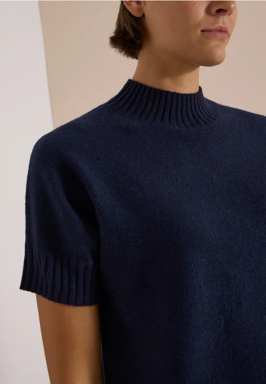 Une personne porte un pull bleu marine à manches courtes et col montant.