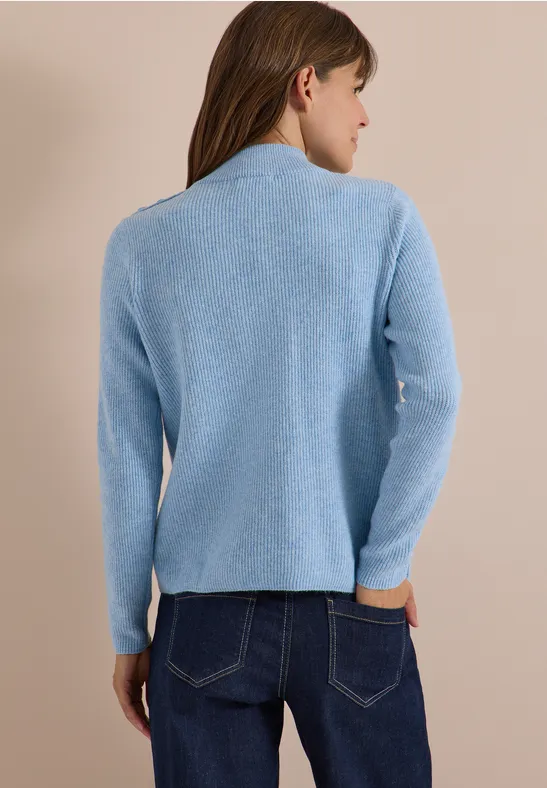 Femme vue de dos portant un pull bleu clair et un jean, fond beige.