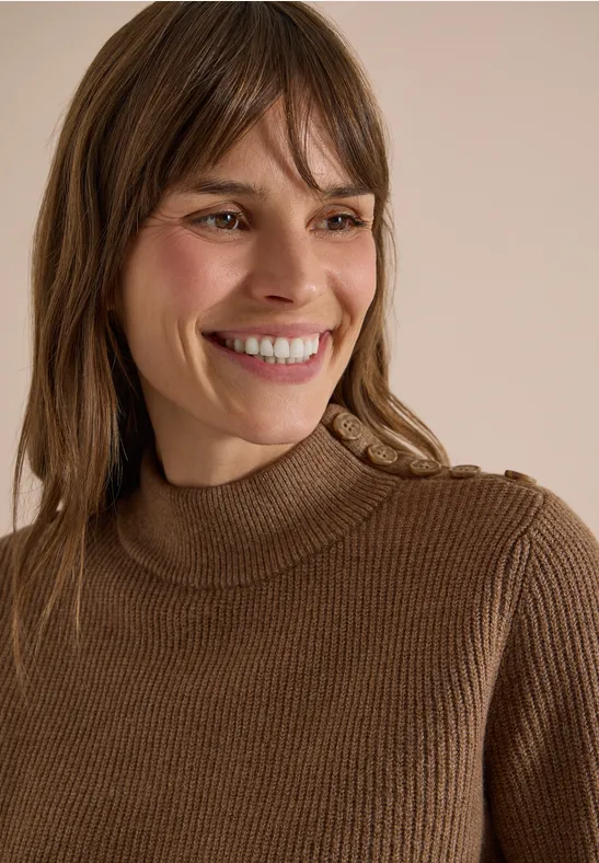Femme souriante en pull à col roulé marron sur fond clair et neutre.